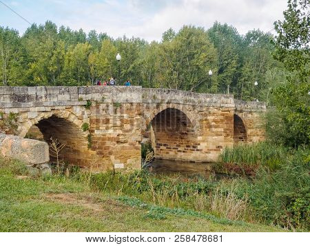 Camino Pilgrims Walk On The Singing Bridge (puente Canto), An 11th Century Stone Arched Bridge, Over
