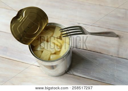 Opened Tin Can Of Canned Pineapple Pieces.  Canned Pineapple In Can With Fork On Wooden Table.