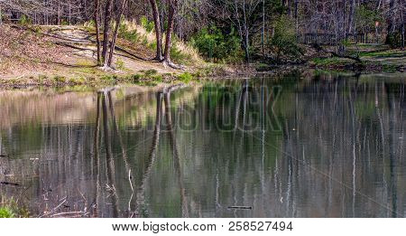 View Of Pond In Winter With Colorful Reflection Of Trees In The Water And Brdige In Background