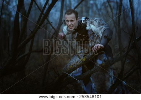 Werewolf With Fangs At Night In The Forest Among The Trees.