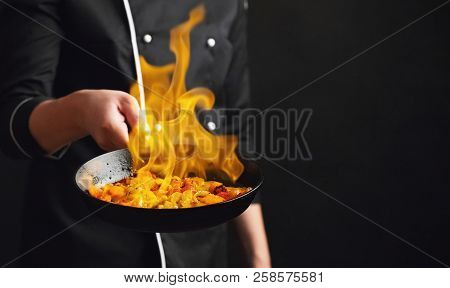 Professional Chef And Fire. Cooking Vegetables And Food Over An Open Fire On A Dark Background. Hote