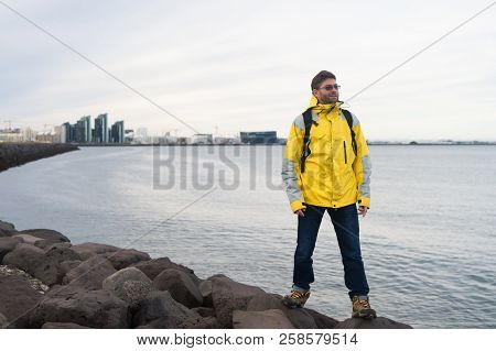 Inspired Man On Sea Beach In Reykjavik, Iceland. Man Traveler Smile And Looking In Future On Sea Sho