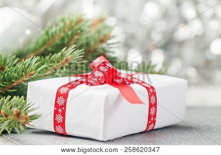 Silver Christmas Background Of Defocused Bokeh Lights With Fir Tree Branches And Gift Box