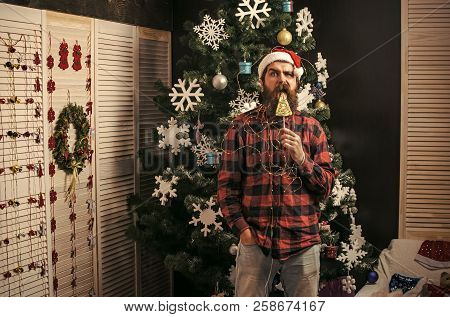 New Year Guy Lick Candy Or Sweet. Winter Holiday And Xmas. Santa Claus Man In Hat At Decoration. Par