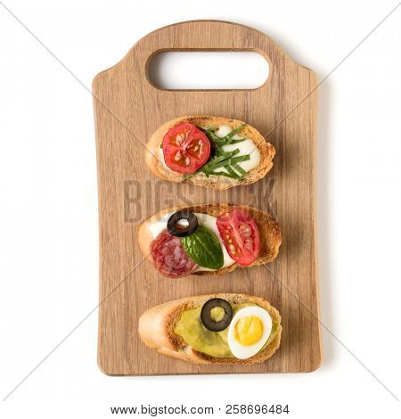 Open faced sandwich canape or crostini on a wooden serving board isolated on white background closeup. Top view.