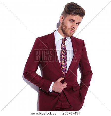 relaxed young businessman holding suits's button looks a little surprised on white background