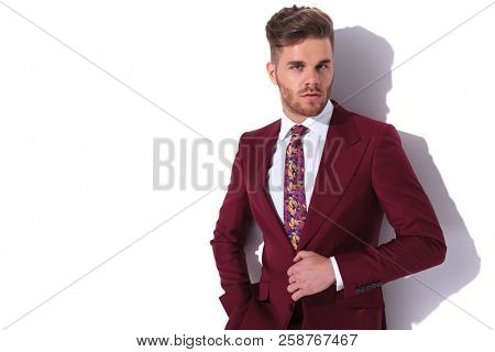 portrait of a handsome elegant man buttoning his burgundy suit and looks to the camera on white background