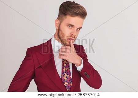 attractive young businessman touching his lips with finger and looks to the camera, studio picture