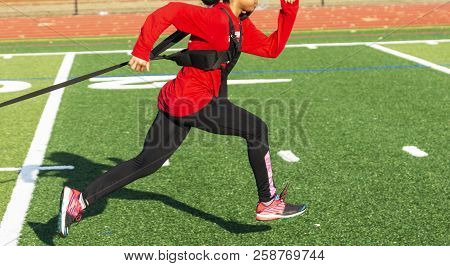 A High School Track And Fiield Girl Is Pulling A Weighted Sled Across A Green Turf Field At Practice