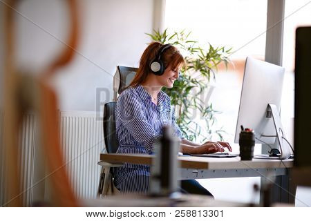 Businesswoman with headphones working at professional computer in office