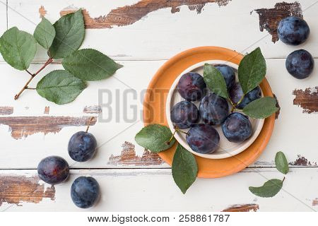 Fresh Plum Berries On A Plate With Leaves On A Light Table.