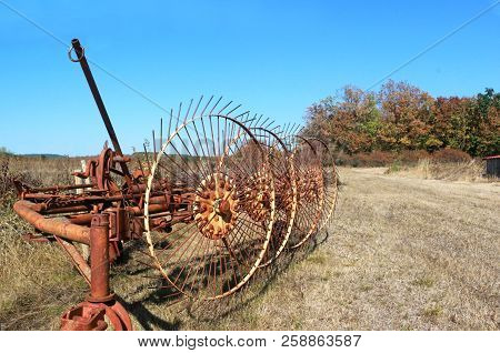 Old Rusty Tedder Standing On A Dry Field In Autumn