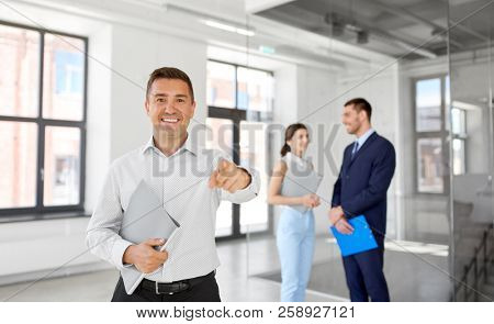 real estate business, sale and people concept - happy smiling realtor or businessman with folder pointing at you and customers at new office room