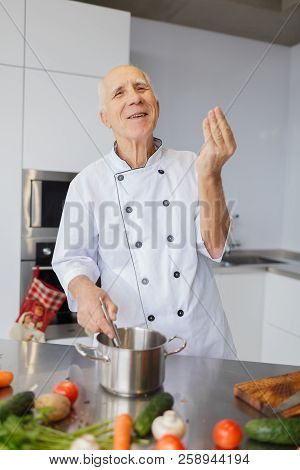 The Aged Chef Man Cooking A Soup In The Kitchen. The Concepy Of Cooking