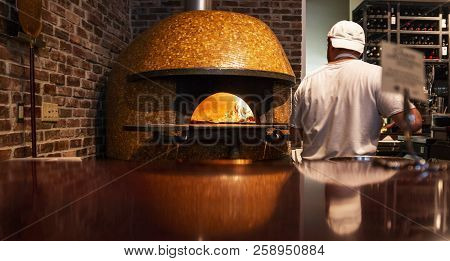 A Chef Is Putting A Handmake Fresh Pizza In A Wood Burning Brick Oven Pizza.