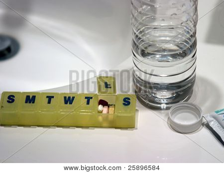 Comprimidos em um contador de comprimido semanal com uma garrafa aberta de água em uma casa de banho