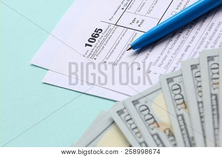 1065 Tax Form Lies Near Hundred Dollar Bills And Blue Pen On A Light Blue Background. Us Return For 
