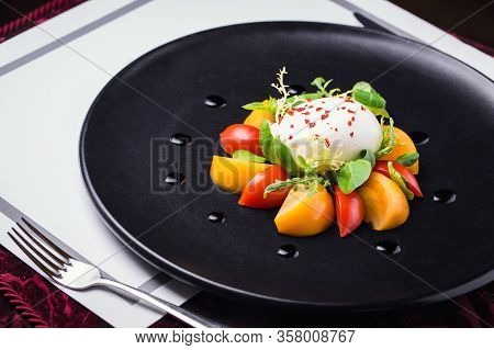 Delicious Buratta Restaurant Dish With Vegetables And Herbs On A Black Plate With A Fork
