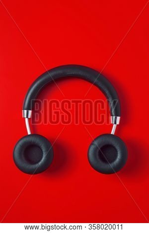 high angle view of a pair of black wireless full size headphones on a red background