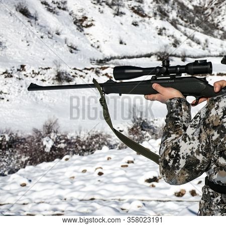 A Hunter In Winter Camouflage Takes Aim At The Optics. A Man In A Winter Camouflage Suit Looks Throu