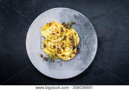 Traditional Italian ravioli pasta offered with capers and onion chili pesto as top view on a modern design plate with copy space 