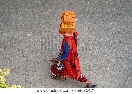 New Delhi, India - March 21, 2020: Indian Woman Wearing A Sari Walks While Carrying And Balancing Br