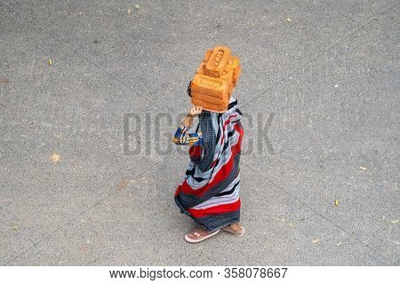 New Delhi, India - March 21, 2020: Indian Woman Wearing A Sari Walks While Carrying And Balancing Br