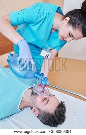 Above view of young nurse using Ambu mask while performing artificial ventilation to mature patient