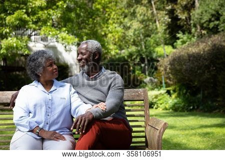 Front view of senior African American couple in the garden, sitting on a bench, embracing and talking. Family enjoying time at home, lifestyle concept