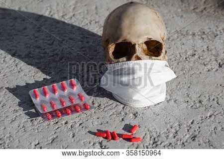 A Human Skull On A Black Background Of Burnt Grass With Red Capsules Of Medical Drugs. A Symbol Of H