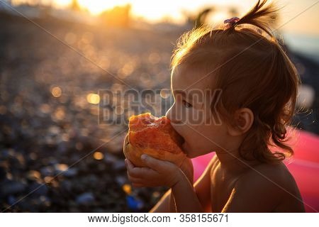 A Little Girl Is Eating A Peach And Is Illuminated By The Golden Light Of The Evening Sun. Girl Bite