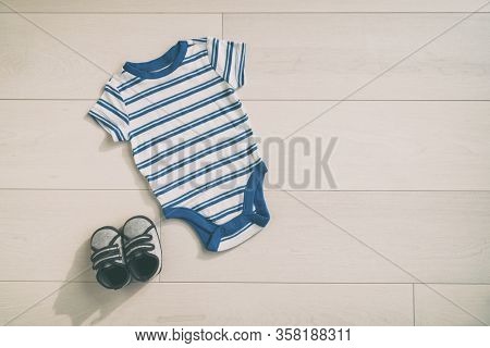 Baby boy outfit newborn onesie clothing with cute little shoes. Clothes in blue stripes style top view on wood floor background.