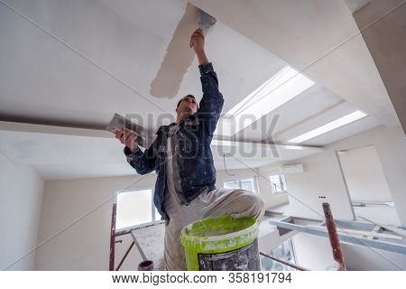young professional construction worker using scaffold while plastering on gypsum ceiling inside the new big modern two levels apartment