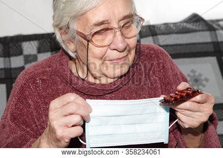 Elderly Woman In A Medical Mask. The Epidemic And Tablets