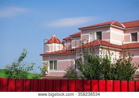 Two-story Brick House With A Red Roof Behind A Red Fencel.