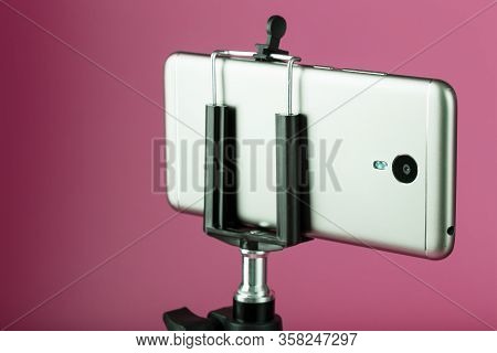 Smartphone On A Tripod As A Photo-video Camera On A Pink Background. Record Videos And Photos For Yo