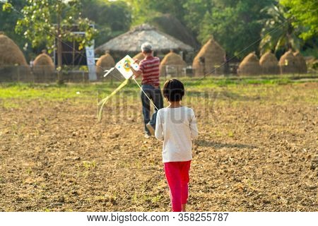 Back Portrait Of Little Asian Girl And Grandfather Play The Traditional Kite In Urban Plaground