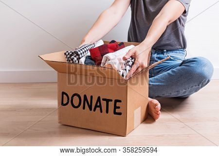Woman Putting Her Clothes In A Carboad Box With Text Donate Written On It.
