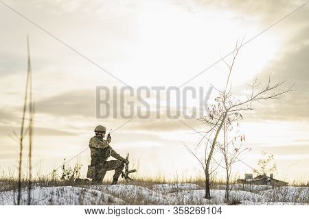 Modern War Soldier Army Man In Camouflage Speaks On The Walkie-talkie Radio Crouching On One Leg In 