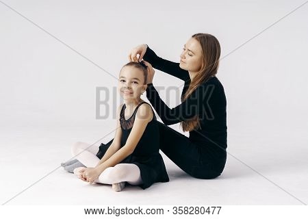 Mother Encourages Her Daughter Ballerina Sitting On The Floor On White Background.