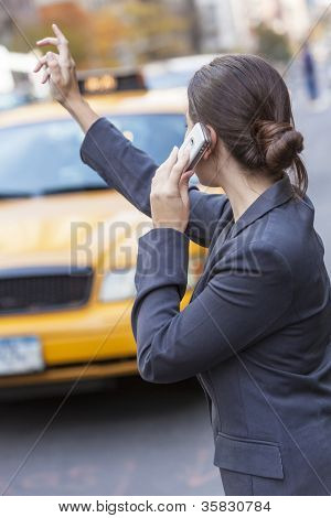 หญิงสาวหรือ businesswoman hailing แท็กซี่มีรถแท็กซี่สีเหลืองในขณะที่พูดคุยในโทรศัพท์ของเธอในสมัย