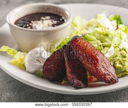 Beautifully Plated Mexican Meal Of Plantains Platanos Beans Sour Cream Lettuce On White Plate On A G