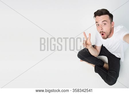 Young Man Isolated Over Background. Guy Take Selfie Alone And Sit On Floor. Emotional Happy With Fac