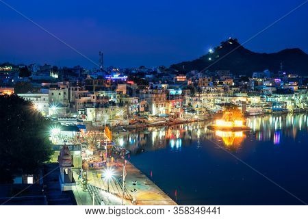 View of famous indian hinduism pilgrimage town sacred holy hindu religious city Pushkar with Brahma temple, aarti ceremony, lake and ghats illuminated at sunset. Rajasthan, India. Horizontal pan