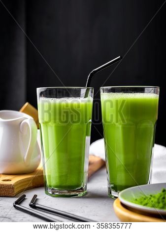 Matcha Green Tea Powder Latte With Milk In Two High Glass On Stone Table, Black Straw, Wooden Plate 