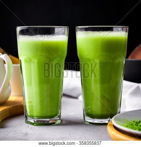 Matcha Green Tea Powder Latte With Milk In Two High Glass On Stone Table, Black Straw, Wooden Plate 