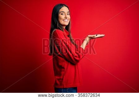 Young beautiful brunette woman wearing casual sweater over isolated red background pointing aside with hands open palms showing copy space, presenting advertisement smiling excited happy