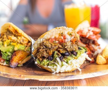 Colombian Arepas Plater With 3 Arepas In The Foreground With Fruit Drinks And Beautiful Brunette You