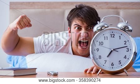 Man in bed frustrated suffering from insomnia with an alarm cloc