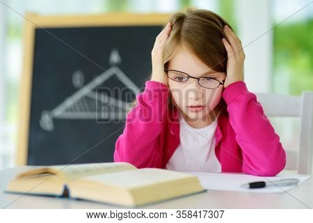 Stressed Schoolgirl Studying With A Pile Of Books On Her Desk. Young Girl Doing Her Homework. Educat